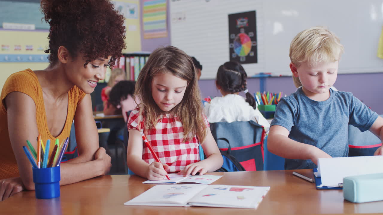 Elementary School Teacher Giving Female Pupil One To One Support In Classroom