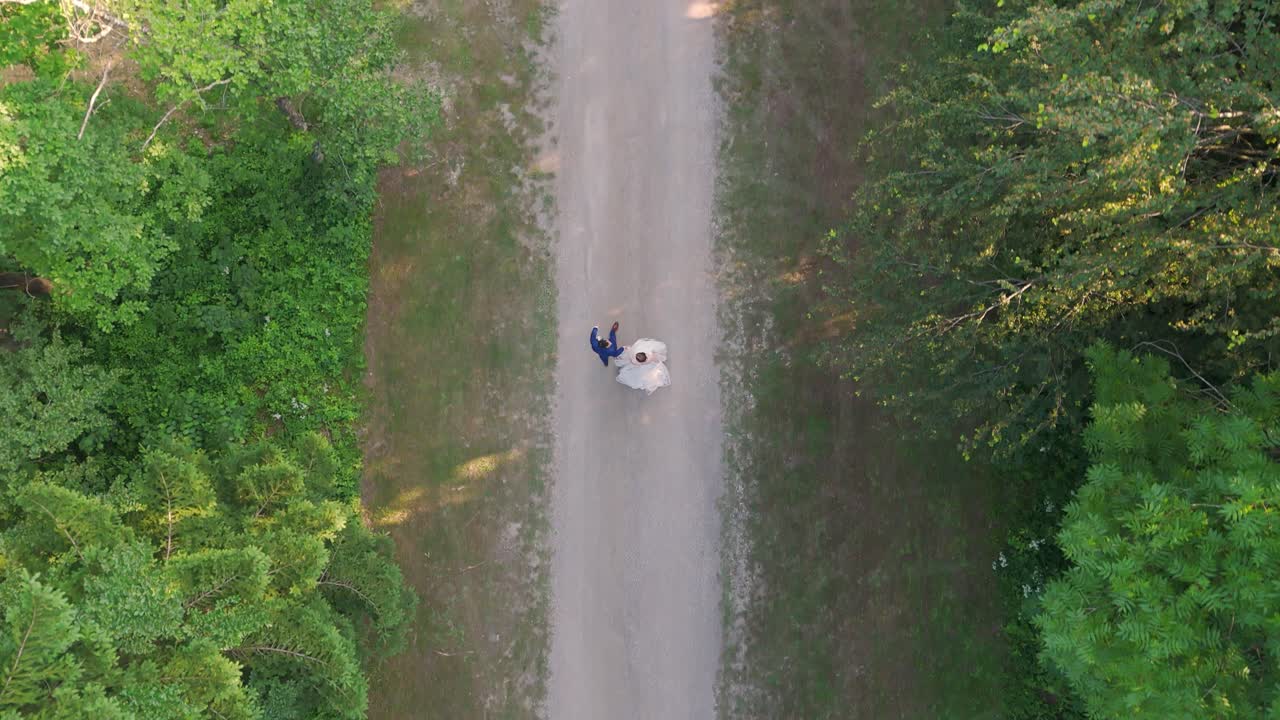 Bride and groom walking along a forest path. Aerial top down