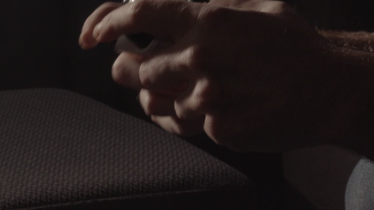 manos jugando agresivamente en un controlador de videojuegos en una sala oscura