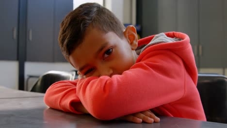 vista frontal de un escolar asiático inclinado sobre el escritorio en el aula de la escuela 4k
