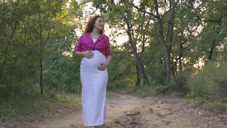 pregnant mom happy exploring forest trail meandering around roots stroking belly