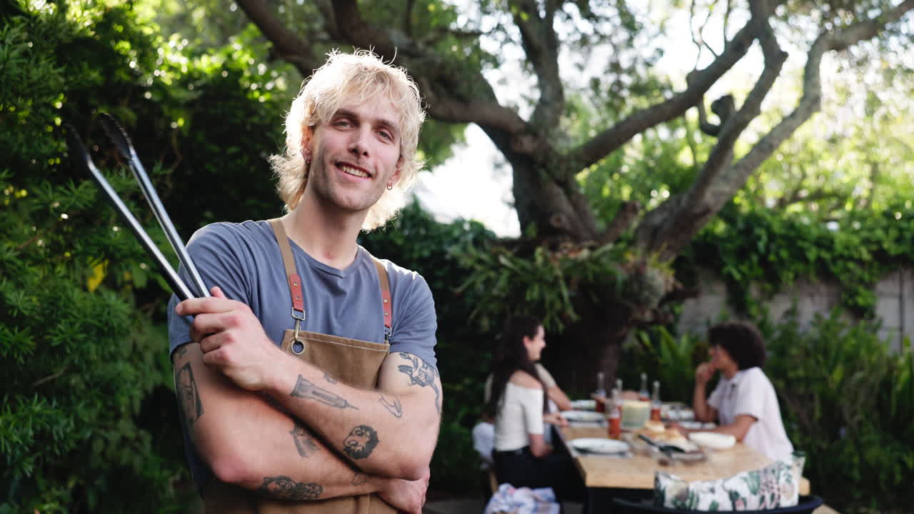 Giovane chef sicuro di sé che sorride con le pinze in un giardino soleggiato