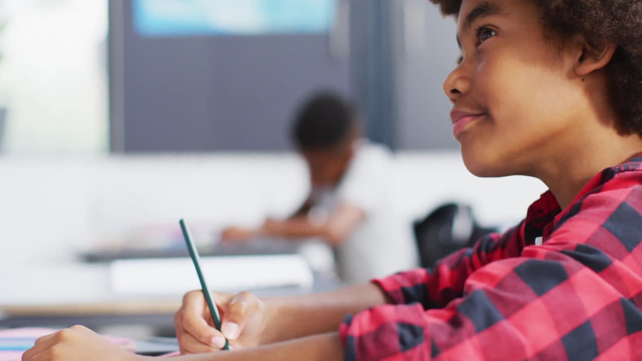 Diverse schoolchildren writing and sitting at desks in school classroom