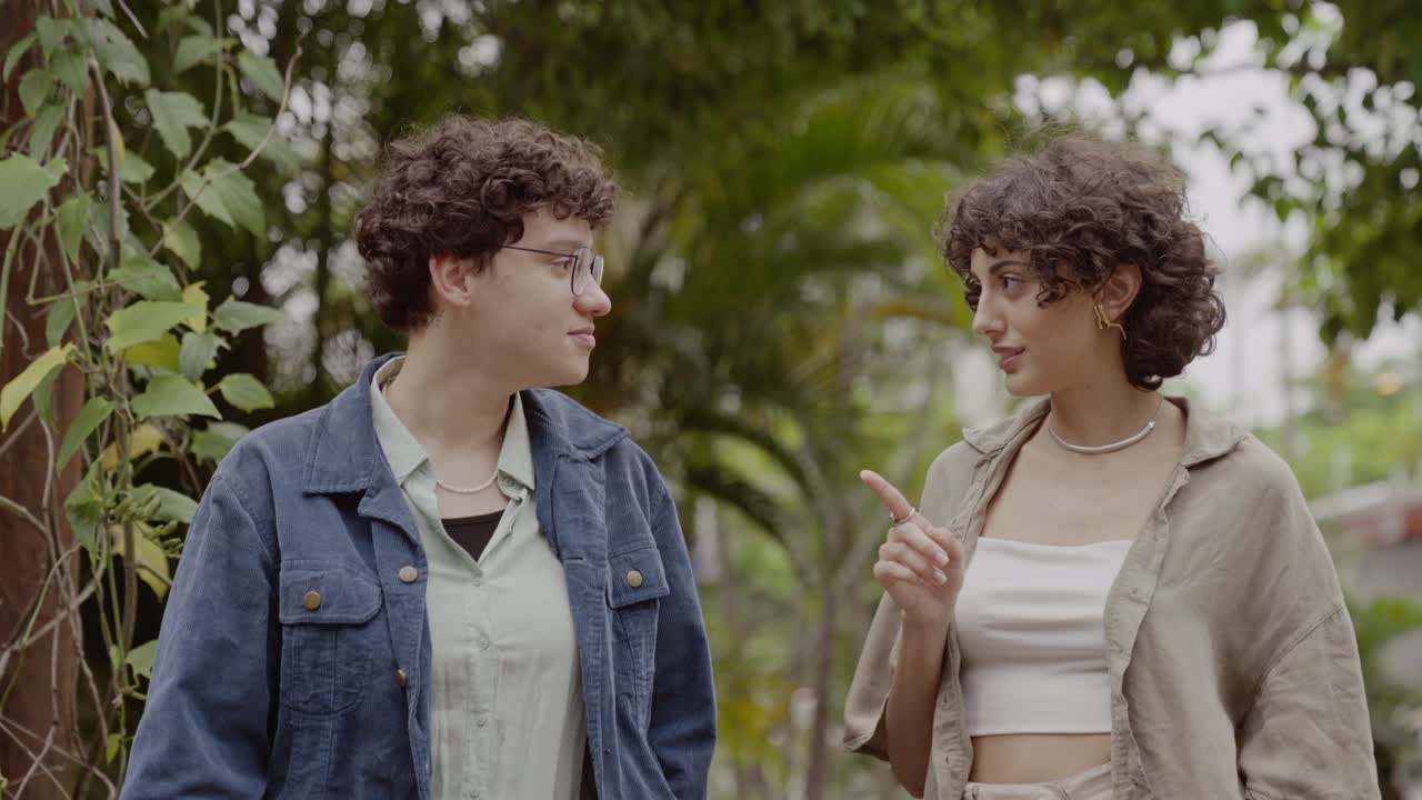 Two young women with curly hair engaging in conversation outdoors