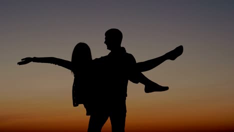 silueta de un hombre que sostiene a una mujer en las manos y la rodea en el cielo al atardecer