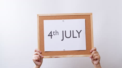 Woman's-hand-shows-the-paper-on-board-with-the-word-4th-JULY-in-white-studio-background-with-copy-space
