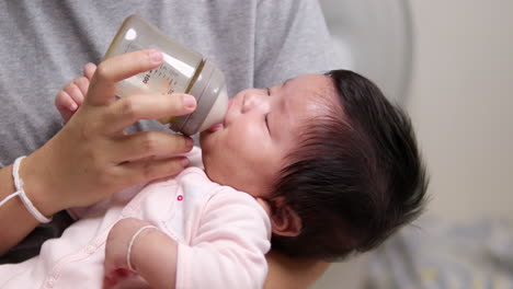 close-up shot of a newborn born child as she is sucking some formula milk from a baby bottle as she is being held in her mother's arms