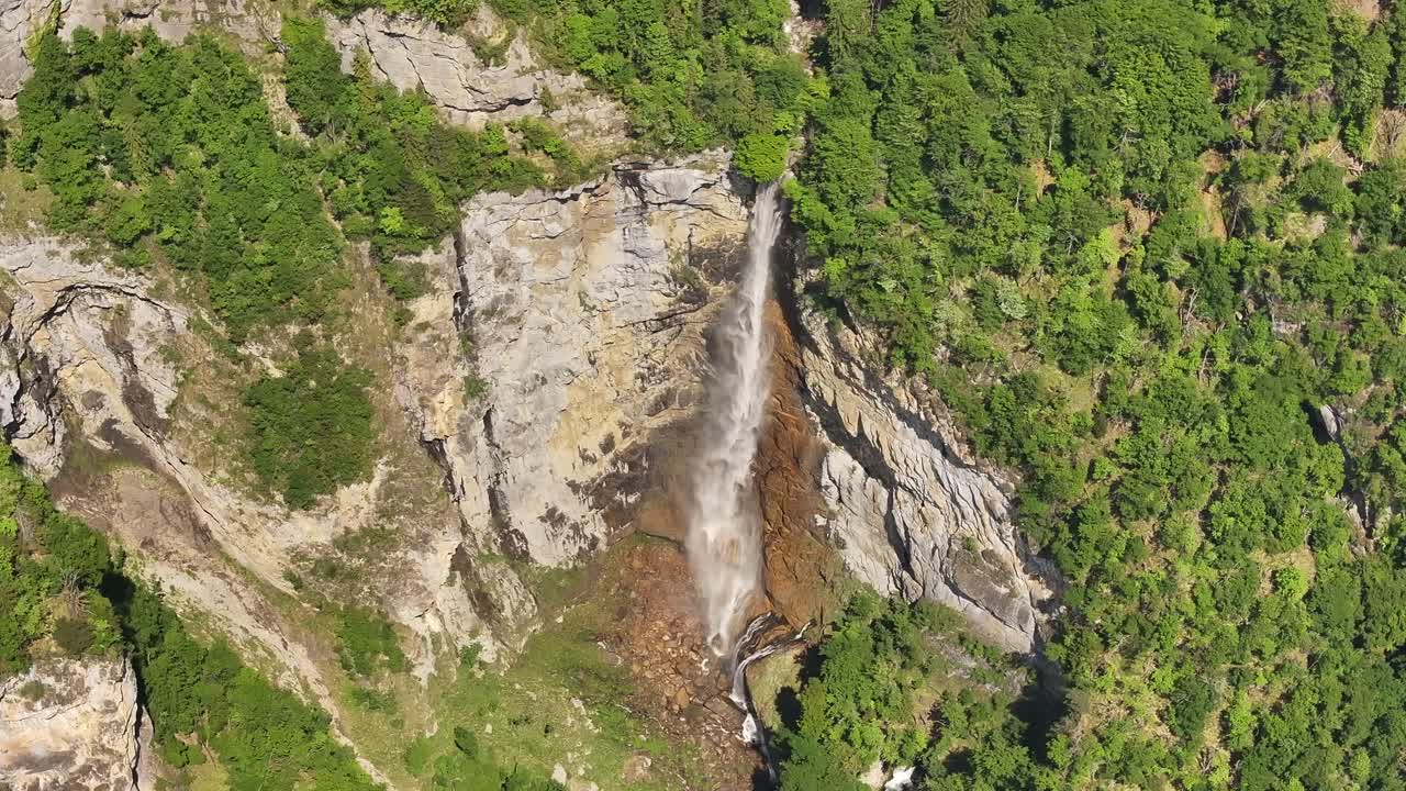 waterfall drops from cliff into rocky base surrounded by dense greenery