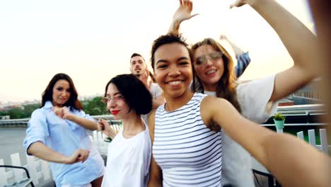 joyful young men and women friends are dancing raising hands and having fun at roof party in summer. modern lifestyle, friendship, leisure and music concept.