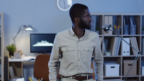 young office worker leaning on the table, then turns his head and smiles to the camera and crosses arms