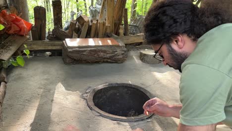 a man is trying to light matches to fire the traditional oven clay oven round circle shape in ground works with wood fire charcoal bone fire camp in order to bake delicious original turkish flat bread