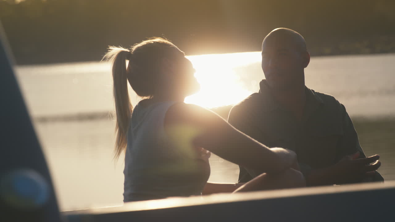 해가 지는 동안 호수 를 따라 도로 여행 을 하는 트럭 의 뒷면 에 앉아 있는 부부