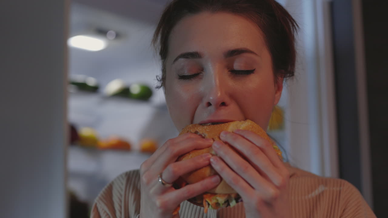 Woman Enjoying a Late-Night Hamburger by the Refrigerator