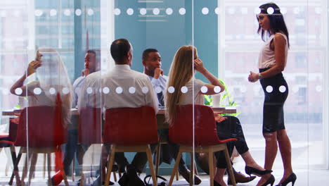 Female-boss-stands-addressing-colleagues-at-business-meeting