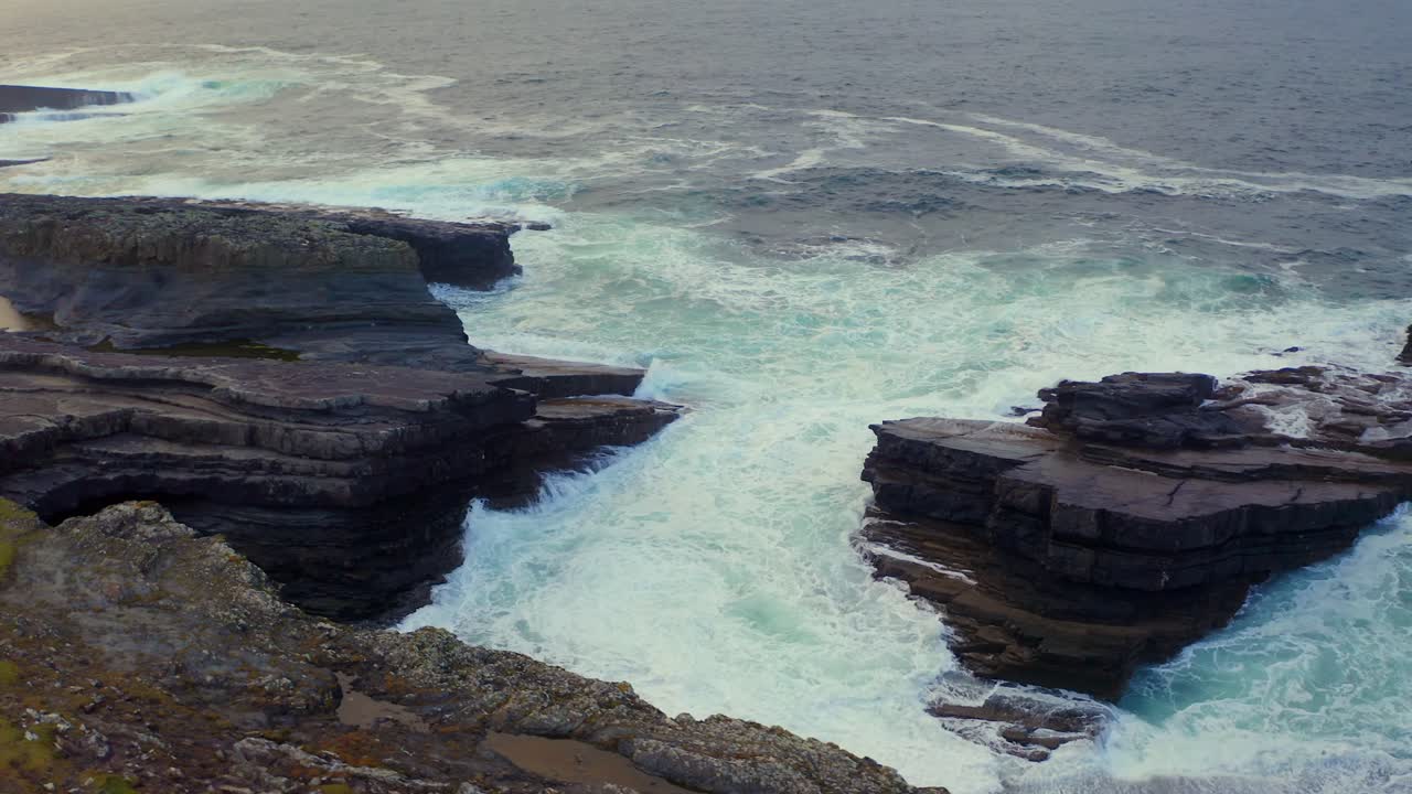 Aerial orbit over stratified limestone at Bridges of Ross with crashing waves. Clare, Ireland