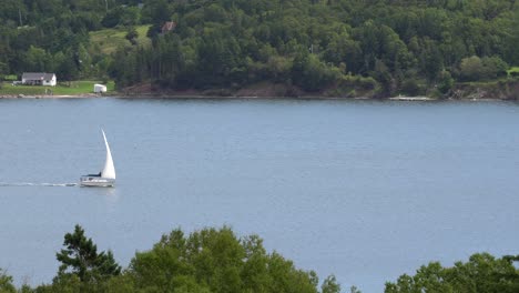 a white sailboat moving slowly on a lake in the distance