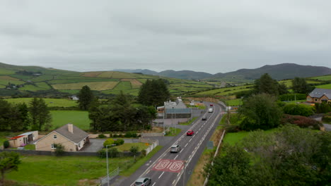 Forwards-tracking-of-group-of-vehicles-driving-on-road-and-passing-through-village-in-countryside.-Landscape-panorama.-Ireland