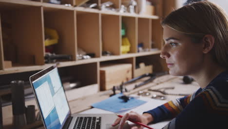 Nahaufnahme-Einer-Ingenieurin-In-Der-Werkstatt,-Die-Einen-Laptop-Benutzt-Und-Sich-Notizen-Zum-Fahrradplan-Macht