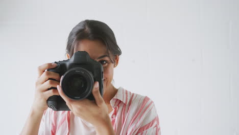 Female-Photographer-With-Camera-On-Photo-Shoot-Against-White-Studio-Backdrop