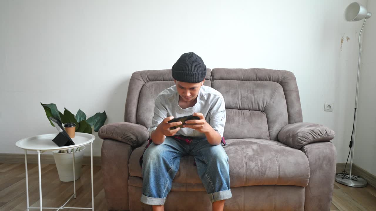 Asian Young Man Presses Buttons On Mobile Phone Quickly While Playing Video Games At Home