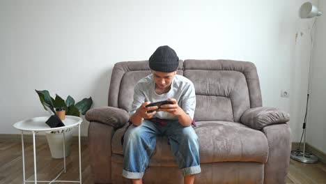 asian young man presses buttons on mobile phone quickly while playing video games at home