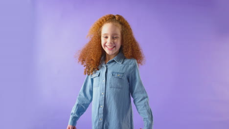 studio portrait of girl with red hair laughing and spinning against purple background