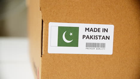 hands applying made in pakistan flag label on a shipping cardboard box with products. close up shot with premium quality barcode