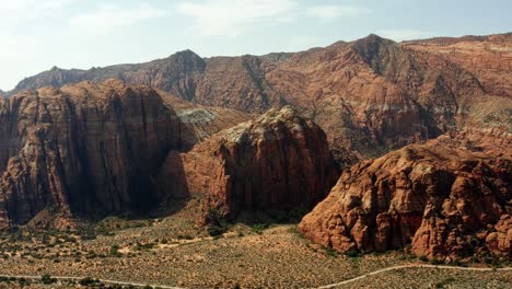 Beautiful-aerial-drone-landscape-nature-left-trucking-shot-of-stunning-red-rock-formations-with-dried-petrified-sand-dunes-below-on-a-hike-in-Snow-Canyon-State-Park,-Utah-on-a-warm-sunny-summer-day