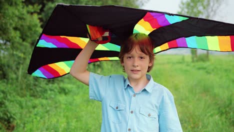 close-up view of a little boy holding a kite and looking at the camera in the park on a sunny day