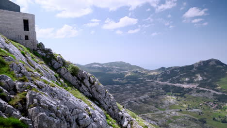 the stone building of the njegos mausoleum atop the mount lovcen in montegro, above a steep rocky mountainside, with a scenic view of the sunlit valleys and mountains below, scenic pan 4k shot