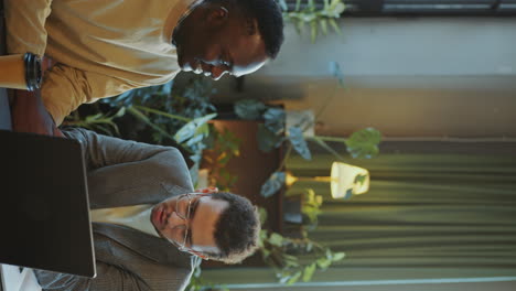two young men talking about business presentation on laptop in office
