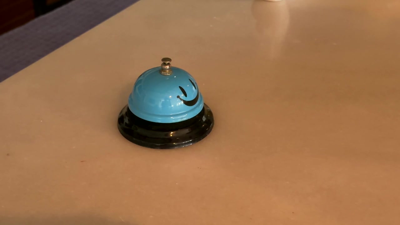 Hand with red painted nails pressing a blue smiley face service bell on a reception counter