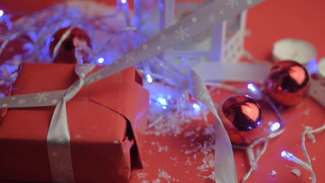 Tying-a-silver-bow-ribbon-on-Christmas-gift-with-red-paper-with-red-background-and-baubles