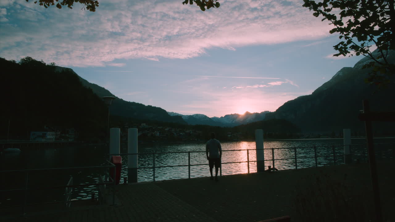 Veltrænet mand beundrer himlen og går langsomt ud på søbroen ved solopgang, mens han strækker armene ud i Brienz, Schweiz i Europa, vidvinkelbillede.