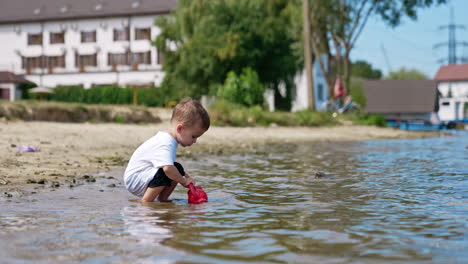 child playing with a toy kettle in the water at the beach