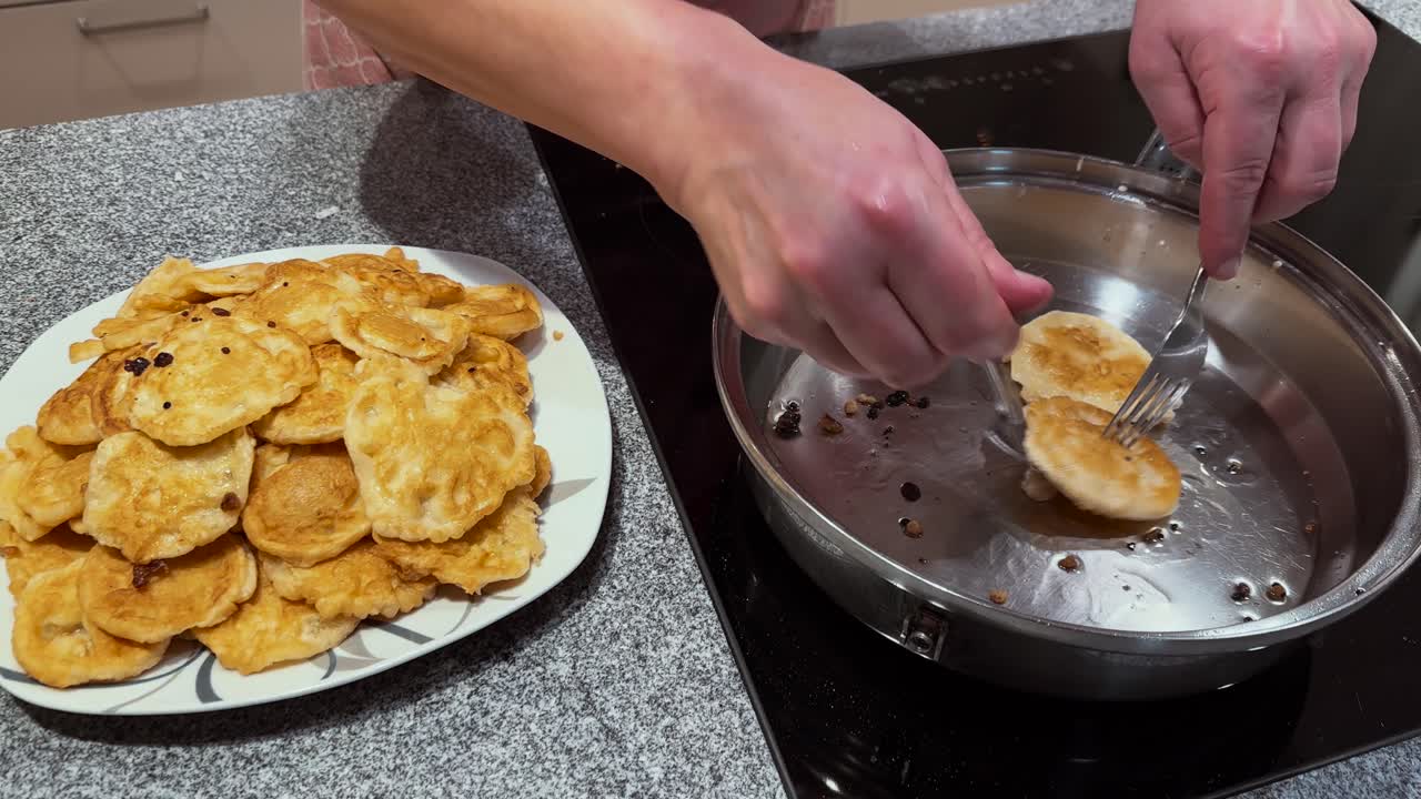 Una persona frigge con cura piccole frittelle in una padella con olio caldo, mostrando cucina casalinga, cautela e preparazione di cibo delizioso fatto in casa