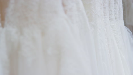 close up of beautiful bridal wedding dresses hanging on rail in shop