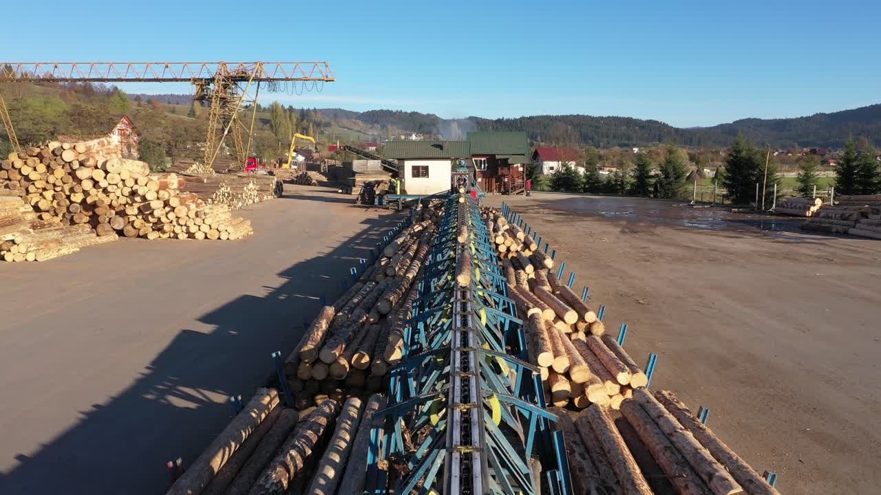 A drone flies over a busy sawmill, a key part of the timber industry. A conveyor system moves fresh logs for processing, with large stacks of raw wood materials ready for production