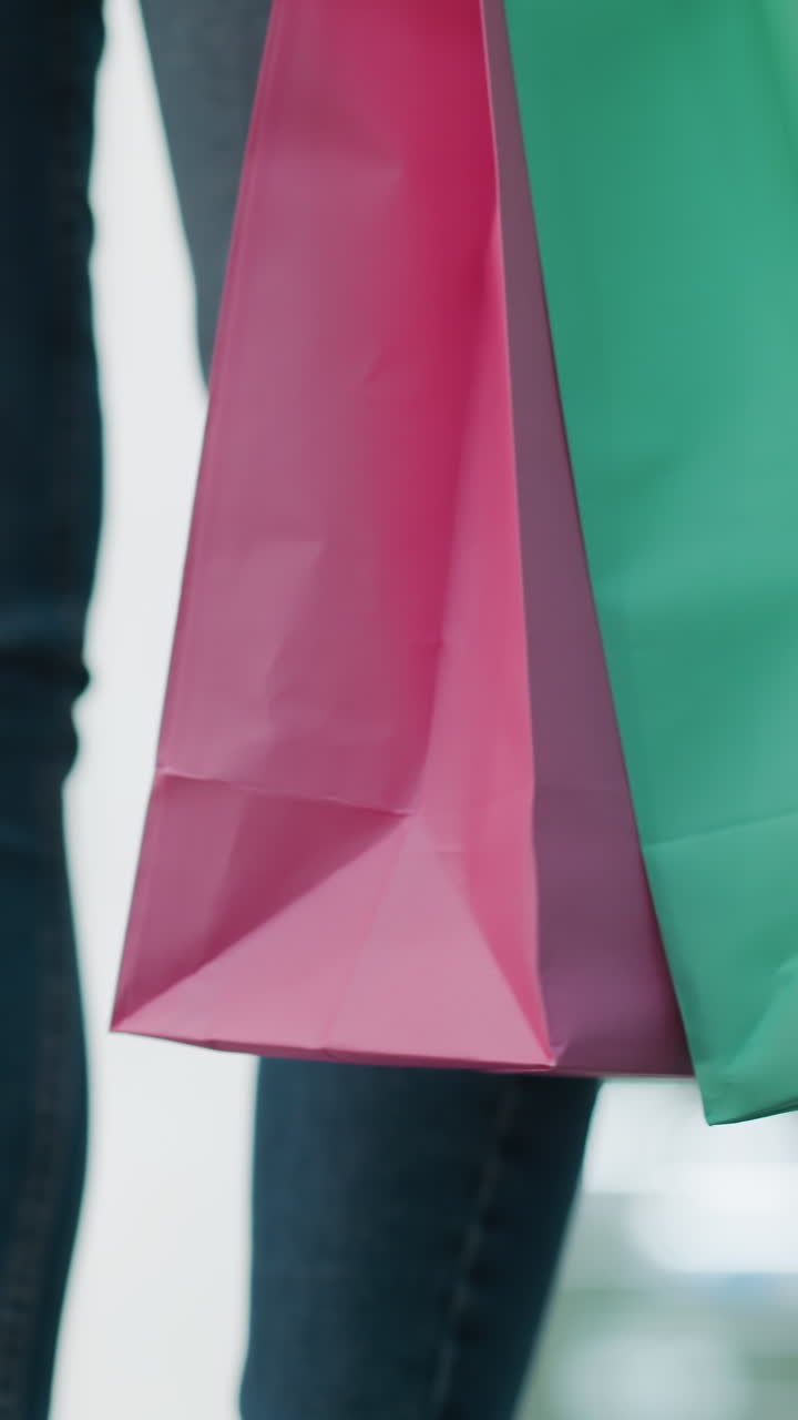 vista parcial de una mujer de pie con bolsas de compras de menta y rosa balanceándose suavemente, con una camiseta de manga larga blanca casual y vaqueros ajustados