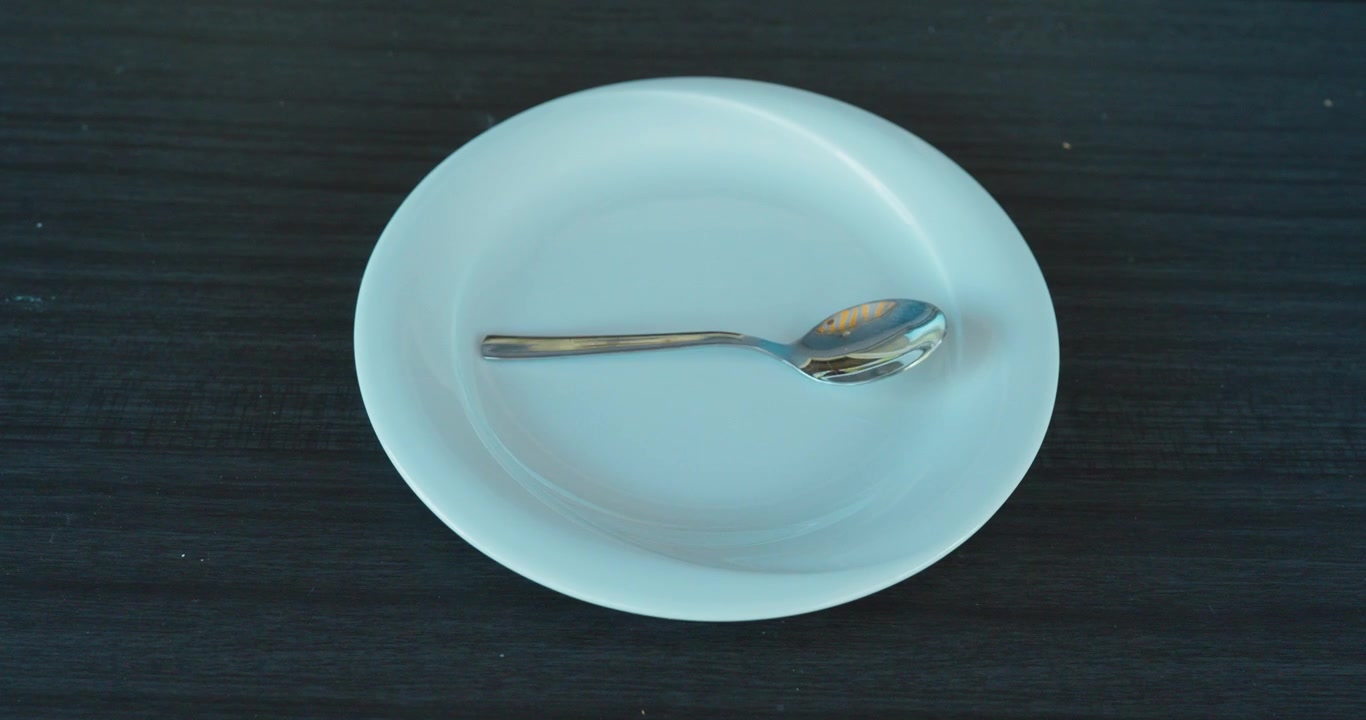 Metal spoon shaking on an empty white plate, representing hunger, food shortage and financial hardship.