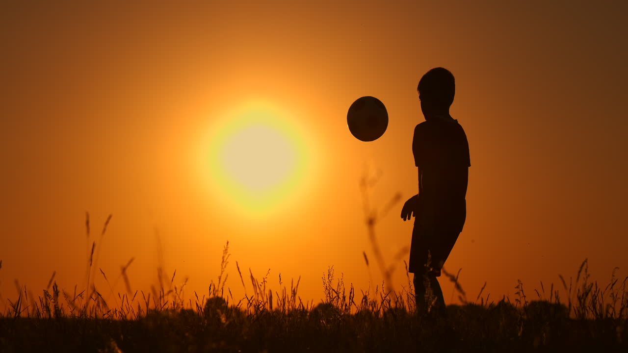 silueta de un niño jugando al fútbol al atardecer. un niño hace malabarismos con una pelota en el campo al atardeecer.