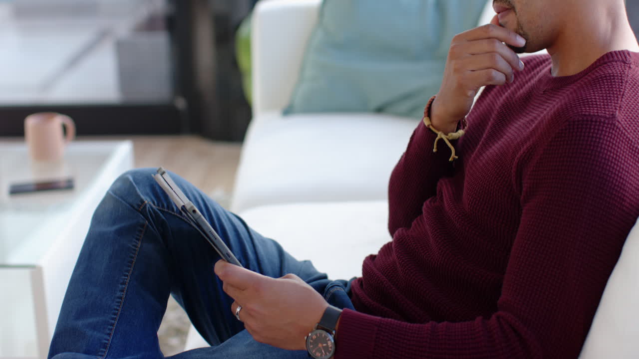 Using tablet, man sitting on couch in casual outfit, relaxing at home