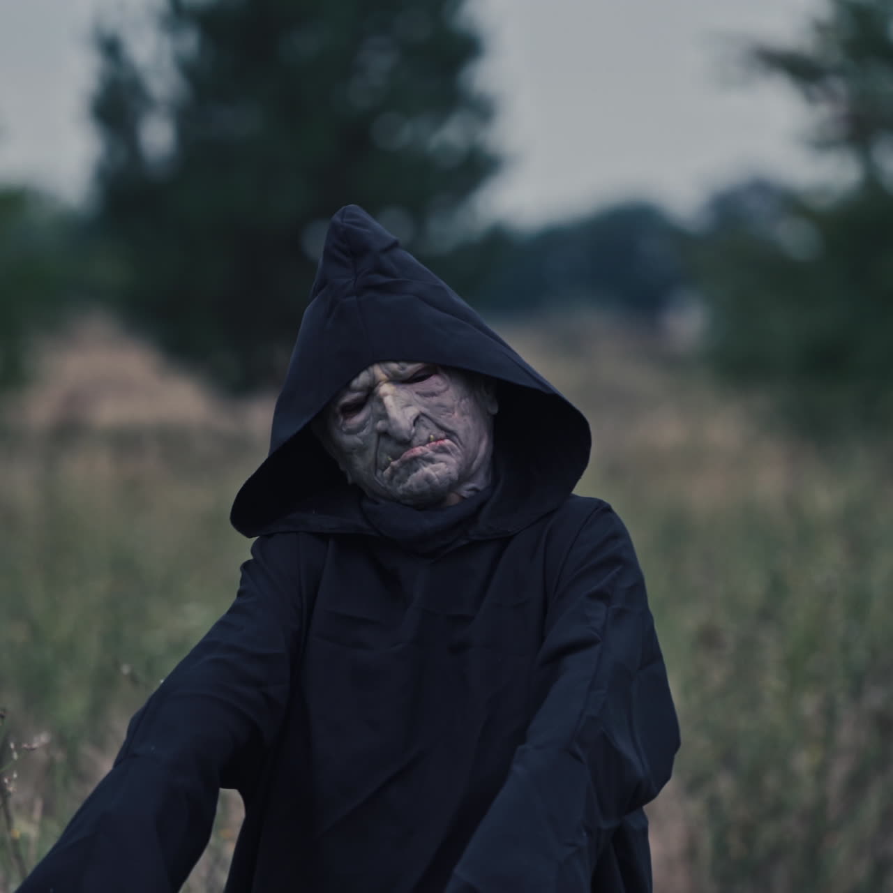 Scary Halloween costume. Portrait of frightful ghost on blur nature background in the evening. Black death in mantle outdoors. Close-up.