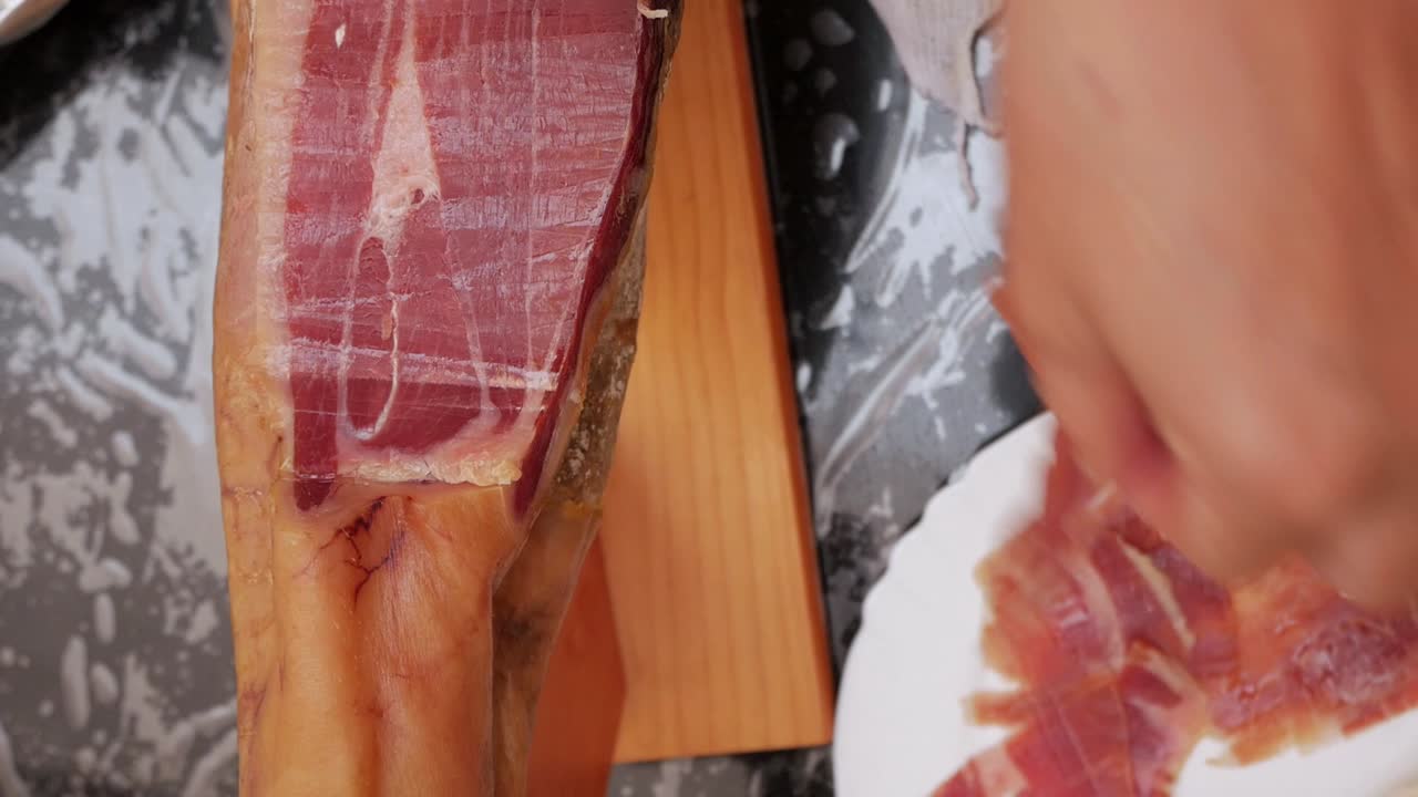 por encima, plano de cerca, jamón español curado siendo cortado con un cuchillo largo y delgado