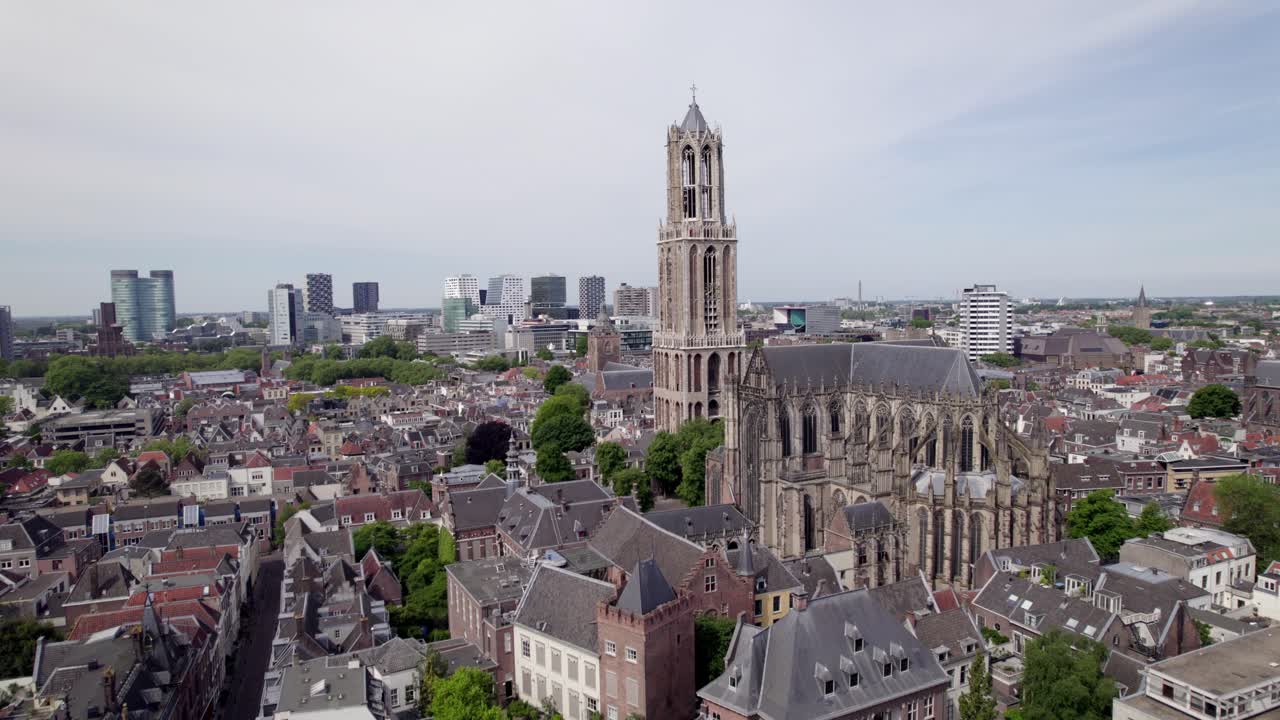 Closeup of De Dom church tower in Utrecht within medieval town and high rise modern buildings on horizon behinc. Holland religious tourist destination seen from above.