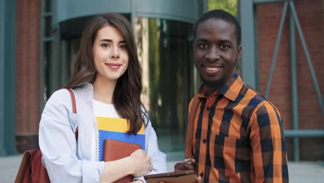 camera zooming on a cucasian woman and african american man watching something on the tablet in the street near the university