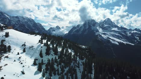 Wide-panorama-flight-above-scenic-Schachenhaus-near-Bavaria-Elmau-castle-away-from-the-snowy-glacier-mountain-tops-in-the-alps-on-a-cloudy-and-sunny-day-along-trees,-rocks,-forest-and-hills-in-nature