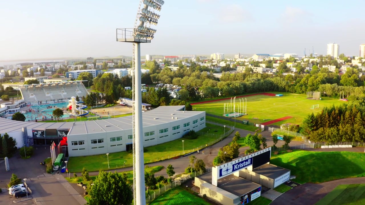 İzlanda'nın Reykjavik şehrindeki Laugardalur spor kompleksinin, güneşli bir günde stadyumu, yüzme havuzunu ve çevredeki şehri gösteren havadan drone görüntüsü