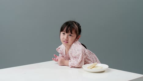 asiatic child eating piece of sweet in studio with gray background