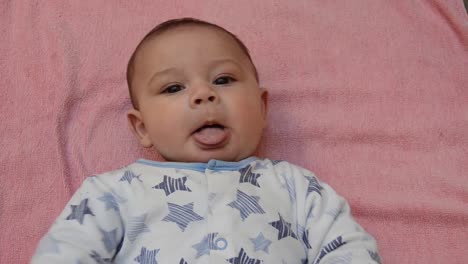 cute tree months old baby boy laying on his back on pinkish towel with teething toy putting his tongue out and kicking with his legs